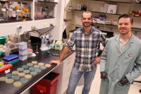two scientists standing next to a lab bench with petri dishes